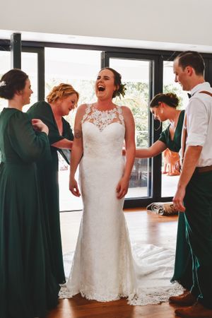 Wedding party sharing a candid moment of laughter with the bride in a lace gown.