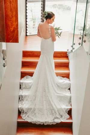 Back view of bride in fitted lace wedding gown with train on wooden staircase.