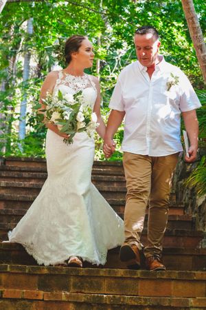 A couple walks down rustic brick steps surrounded by lush greenery in a garden setting.