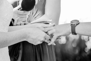 Black and white close-up of hands exchanging rings during a wedding ceremony.