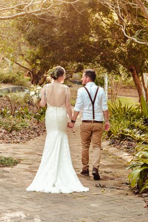 Newlyweds walking hand in hand down a garden path after their wedding ceremony.