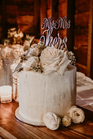 Elegant white wedding cake decorated with roses and a 'Mr & Mrs' topper in a rustic wooden setting.