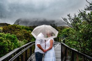 Couple sharing an intimate moment under a white umbrella on a misty boardwalk.