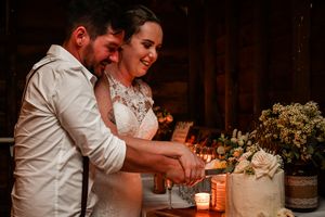 Couple cutting their wedding cake together in a warmly lit rustic venue.