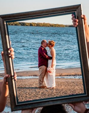 A framed beach wedding photo being held up against the ocean backdrop.