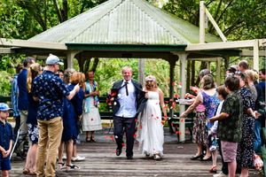 Newlyweds walking through guest-lined pathway under outdoor pavilion during wedding celebration.