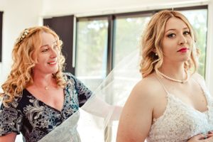Two women in wedding attire sharing a joyful moment indoors.