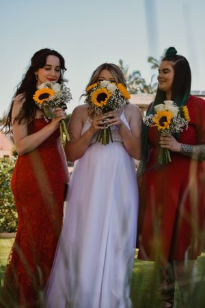 Bridesmaids in red dresses holding sunflower bouquets with bride in white.