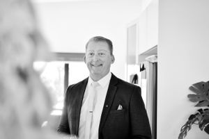 Black and white portrait of person in formal attire smiling in hallway.