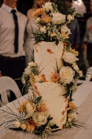 An elegant white wedding cake decorated with fresh roses and greenery in a rustic style.