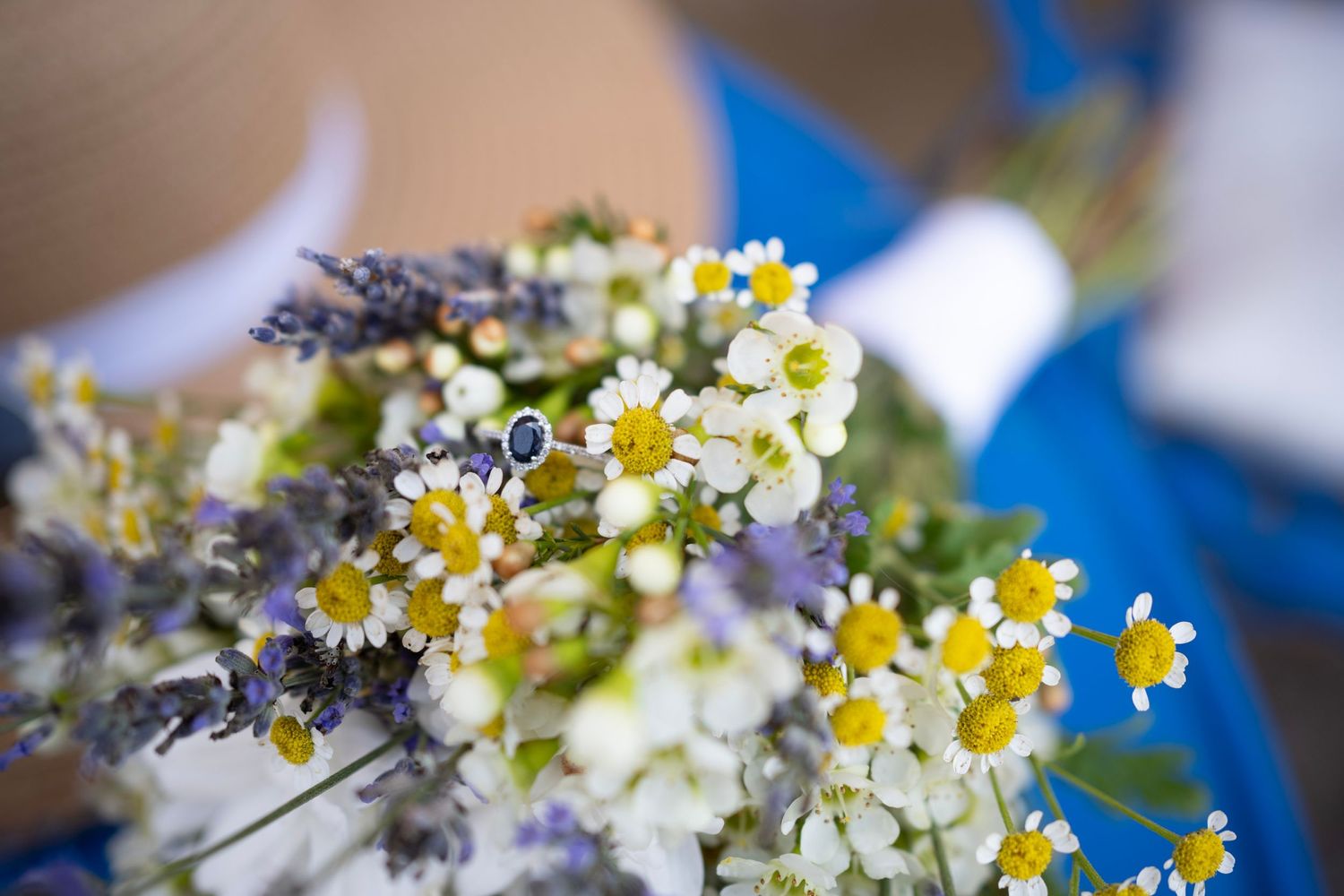 Close-up of delicate white daisies and lavender in a wedding bouquet against blue background.