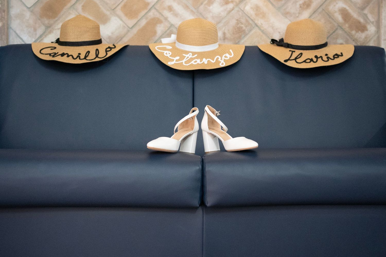 Three straw hats and white wedding shoes arranged on dark blue couch.