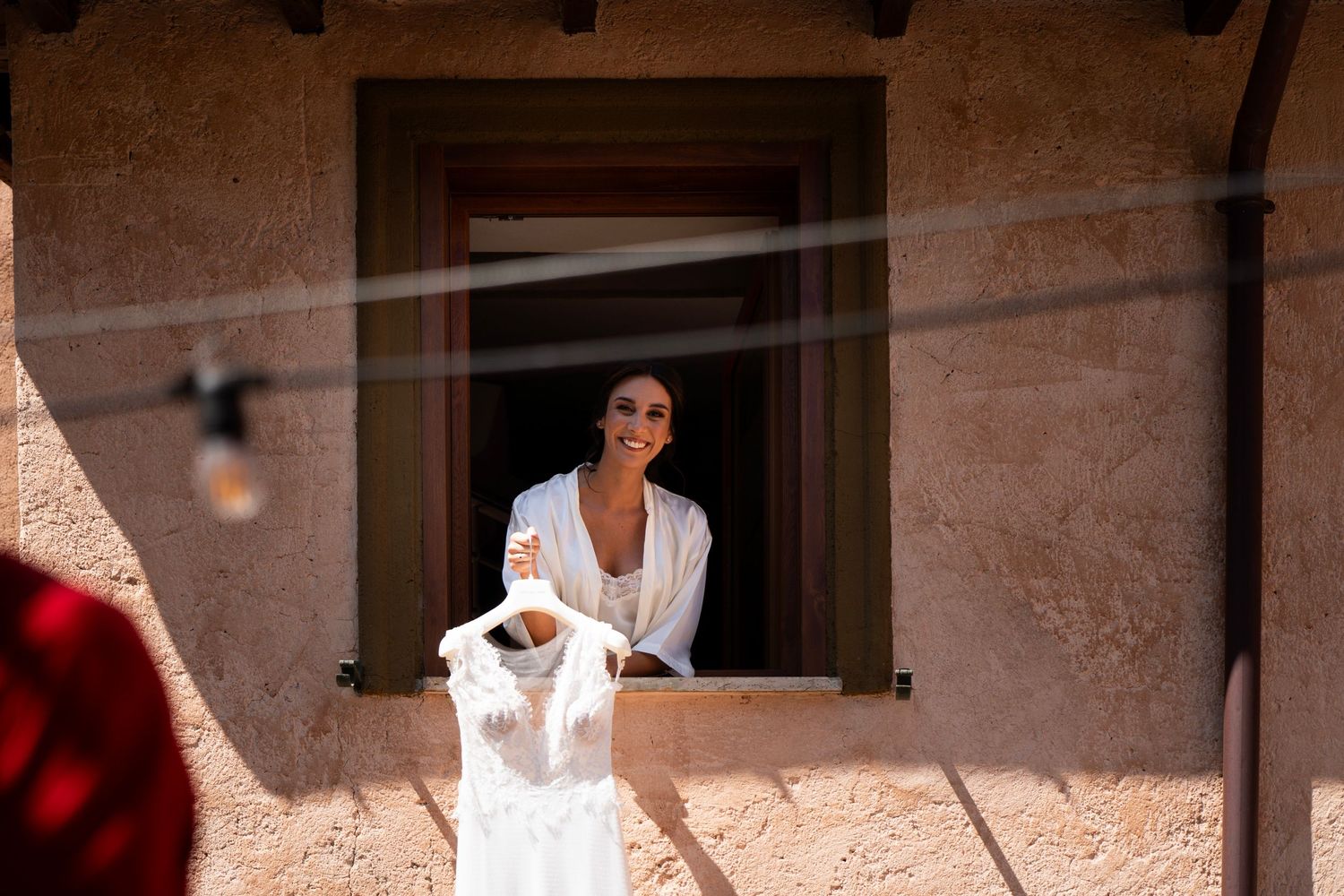 White wedding dress preparation scene through rustic window frame.