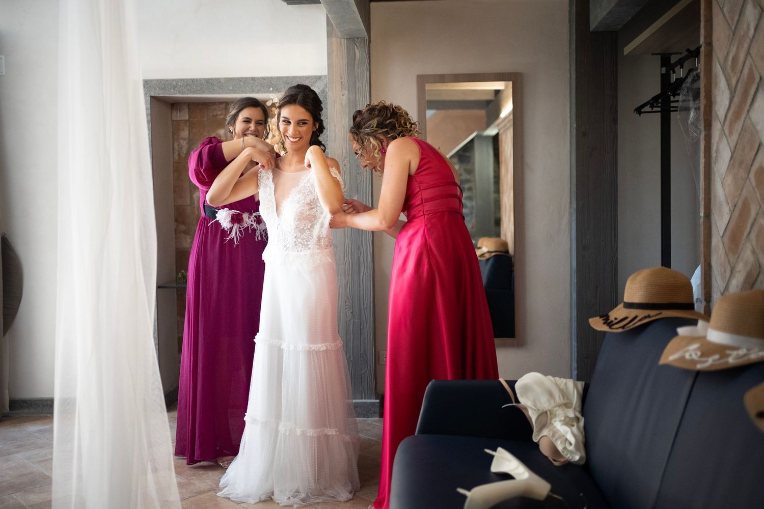Bridesmaids in burgundy dresses assist with final wedding dress preparations.
