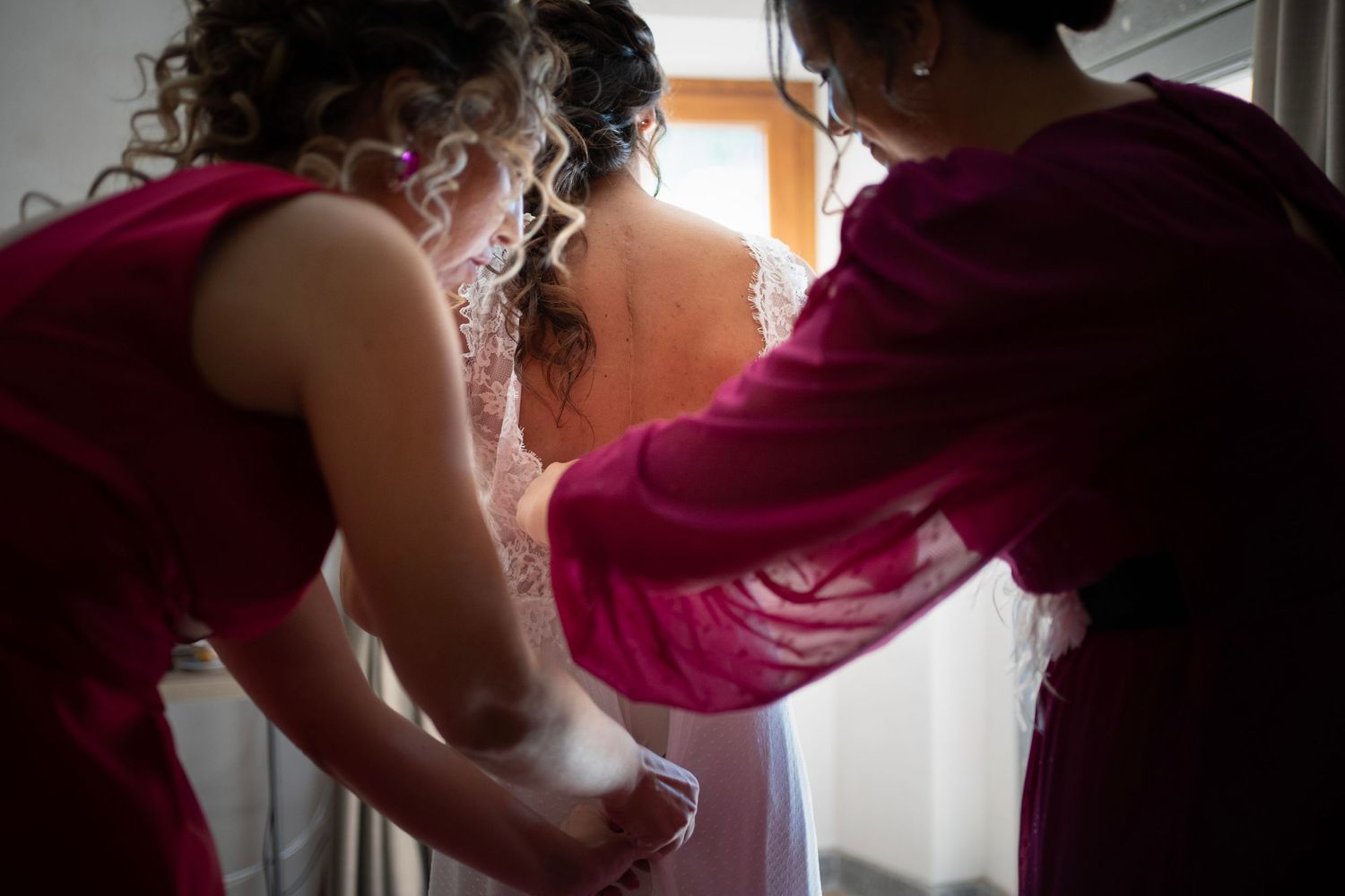 Wedding preparations in progress as attendants help with final dress adjustments.