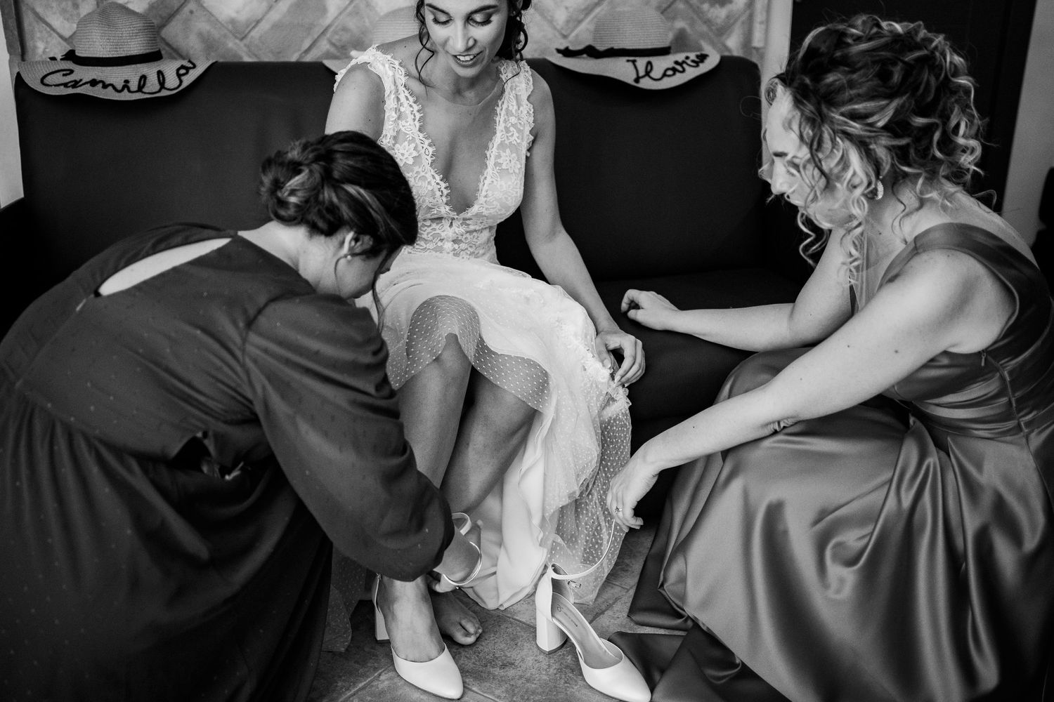 Black and white photo of wedding preparation with attendants helping with shoes.