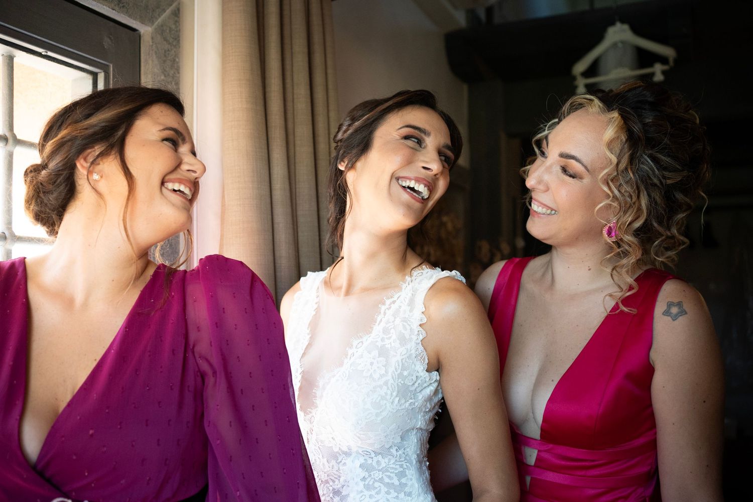 Joyful wedding party moment with bridesmaids in burgundy dresses sharing laughter.
