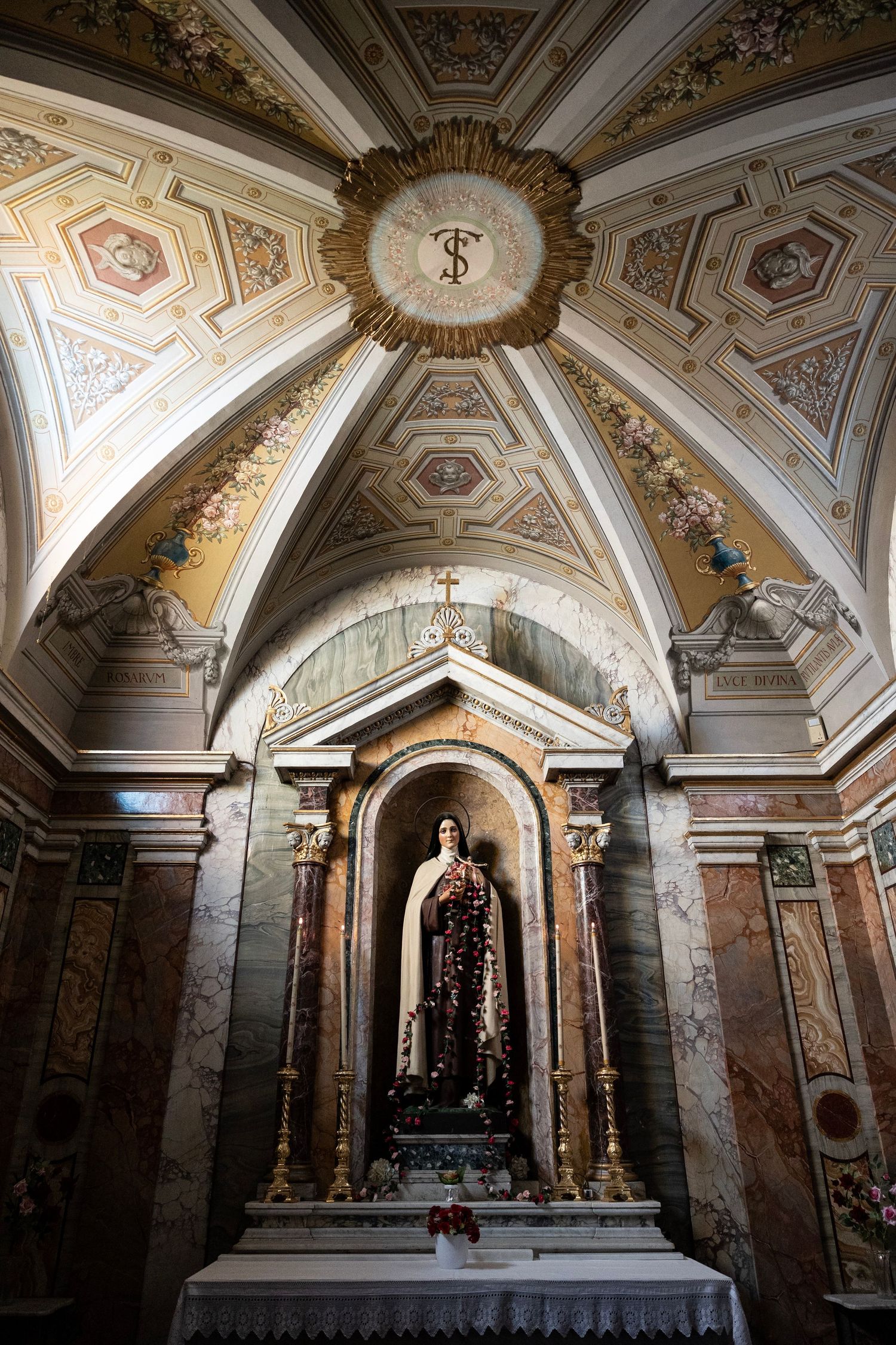 Ornate church chapel interior with decorated dome ceiling and religious statue in an alcove.