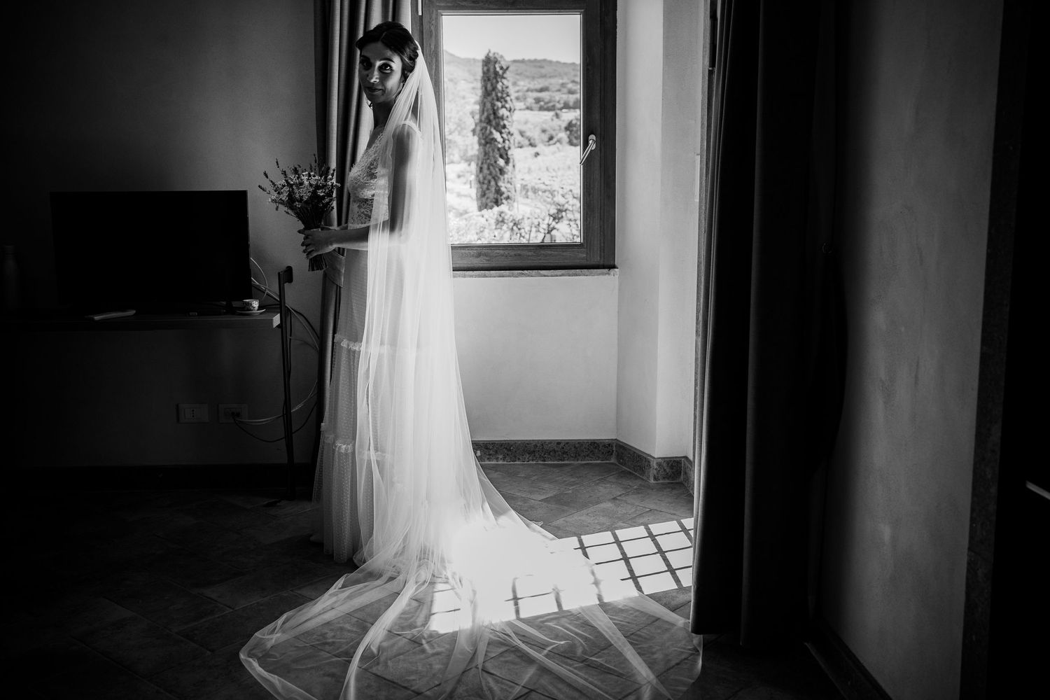 Dramatic black and white bridal portrait with flowing veil in window light.