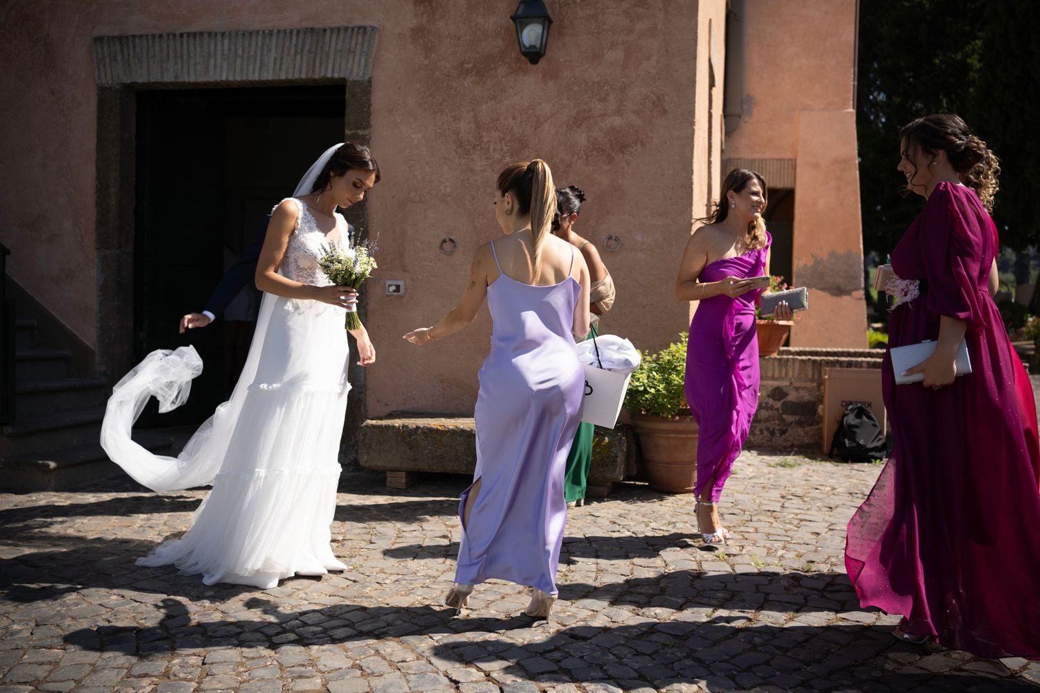 Wedding party in white and magenta dresses dancing in sunny courtyard.