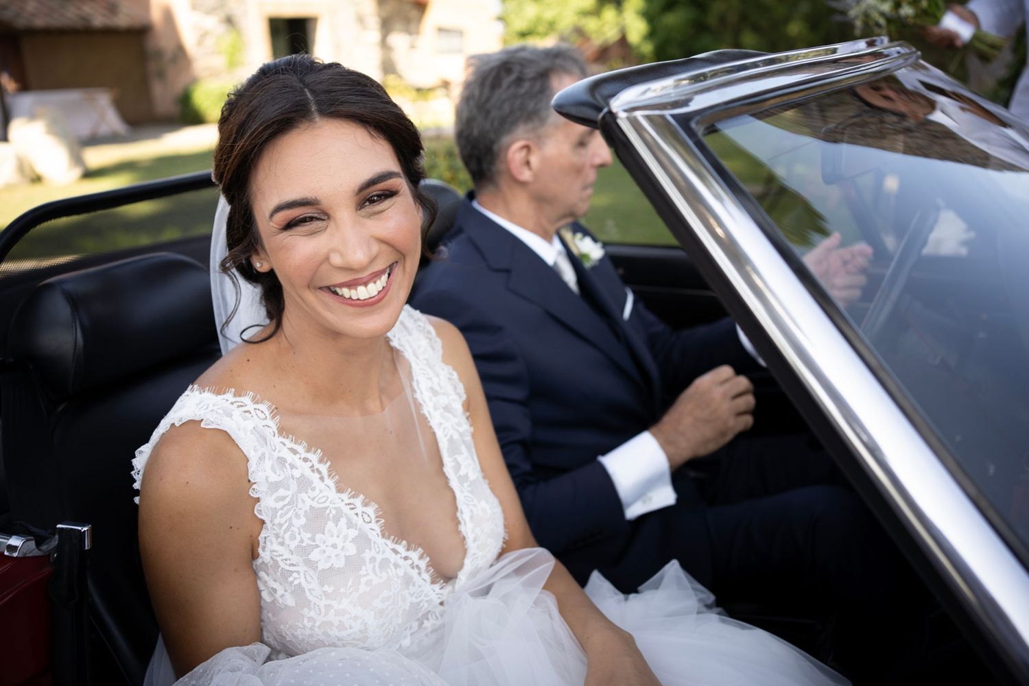 Joyful moment captured in classic wedding car with elegant lace dress details.
