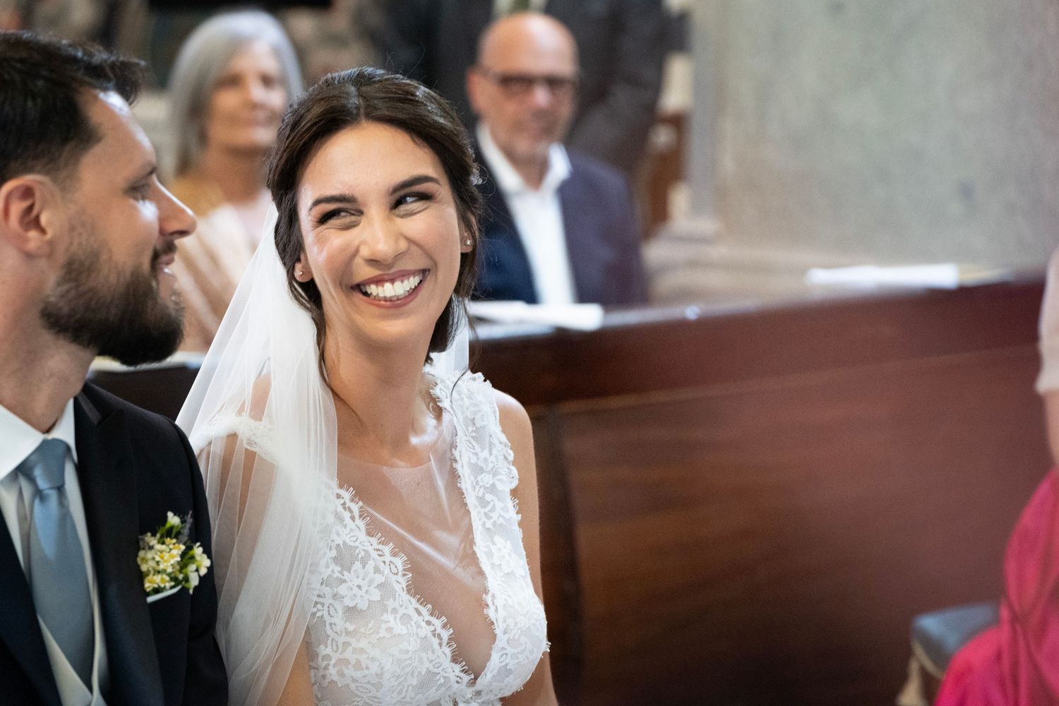 Natural candid moment during wedding ceremony with guests visible in background.