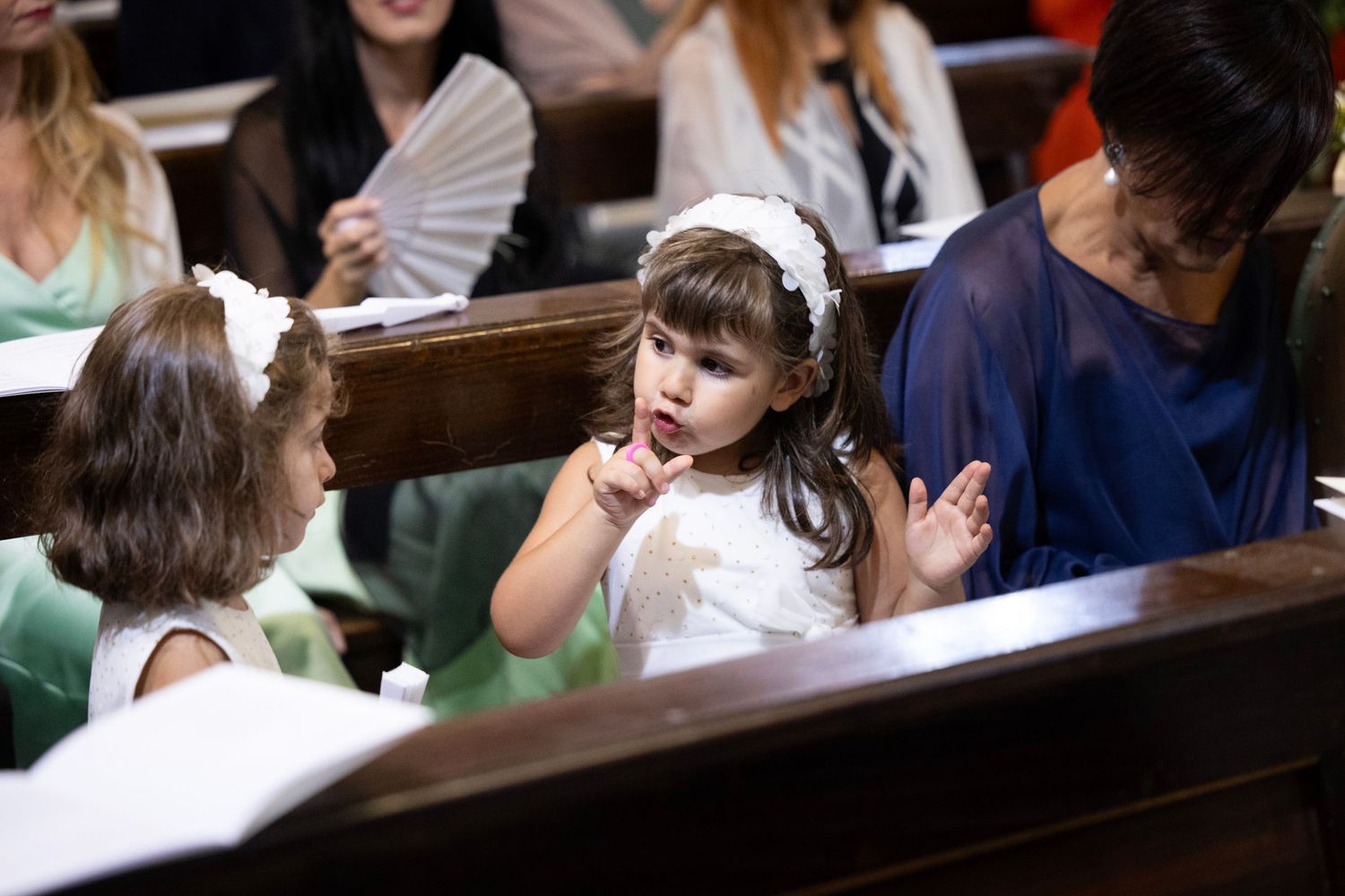 Young attendees interact during church wedding ceremony while seated in wooden pews.