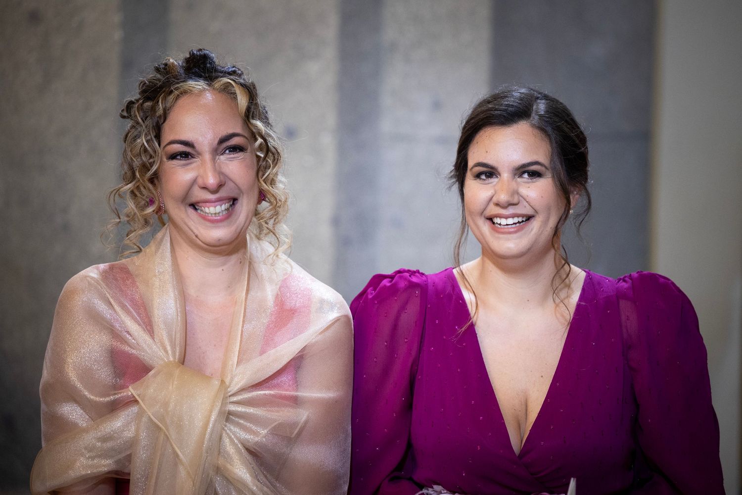 Two event guests smile while wearing elegant pink and purple dresses at a formal gathering.