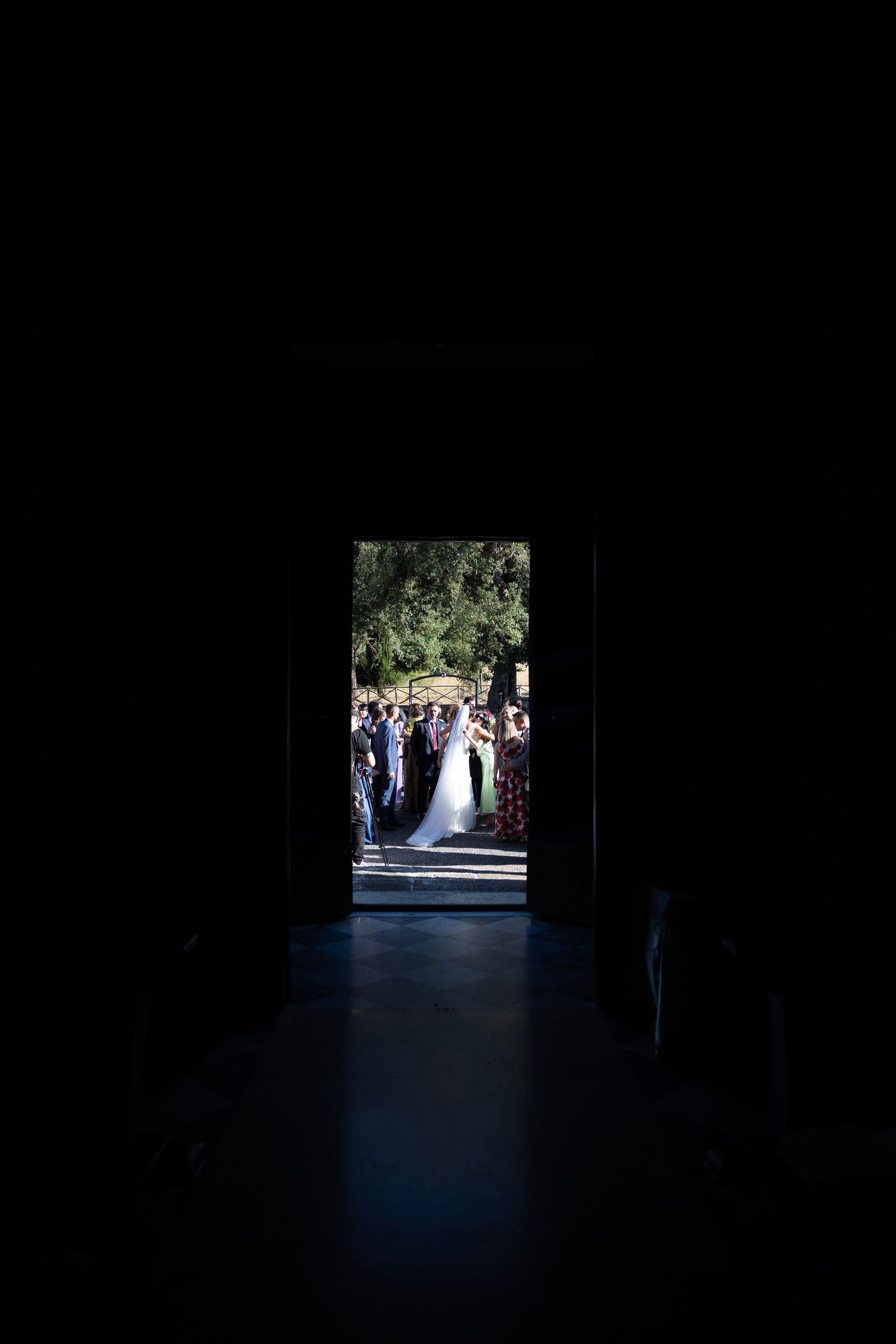 A silhouetted wedding ceremony viewed through a dark doorway frame.