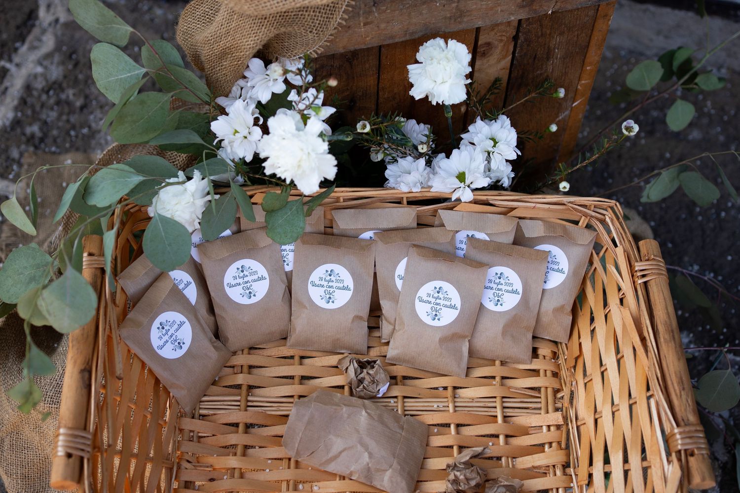 Wedding favor bags decorated with white flowers arranged in rustic wicker basket.