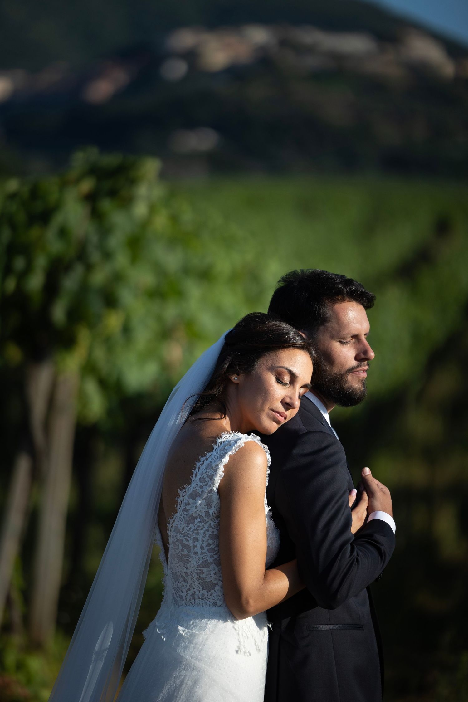 Newlyweds embrace in a romantic pose among vineyard rows at sunset.