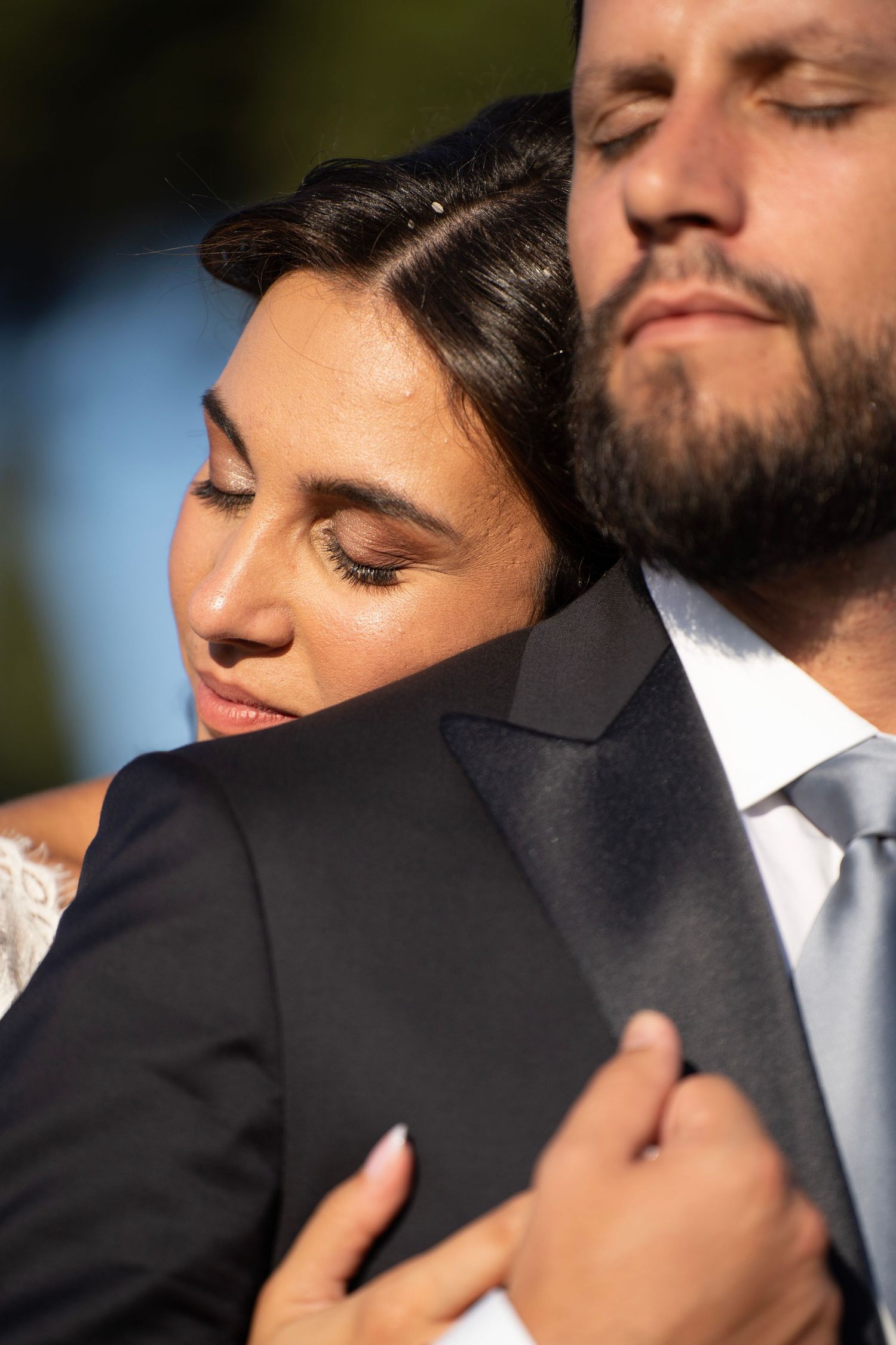 A romantic wedding couple embraces in warm sunlight during an intimate outdoor moment.