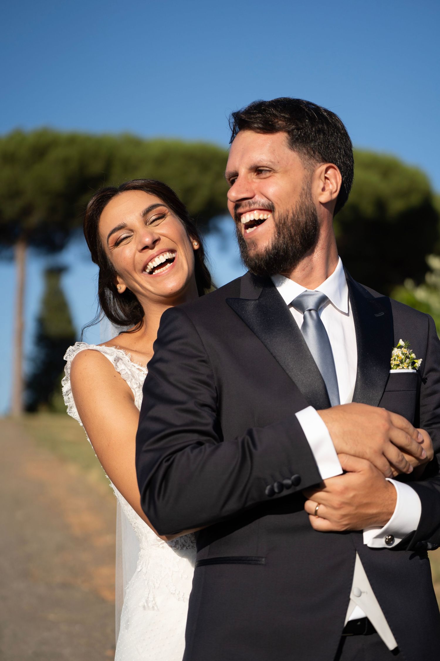 A joyful wedding couple laughing together outdoors on their special day.