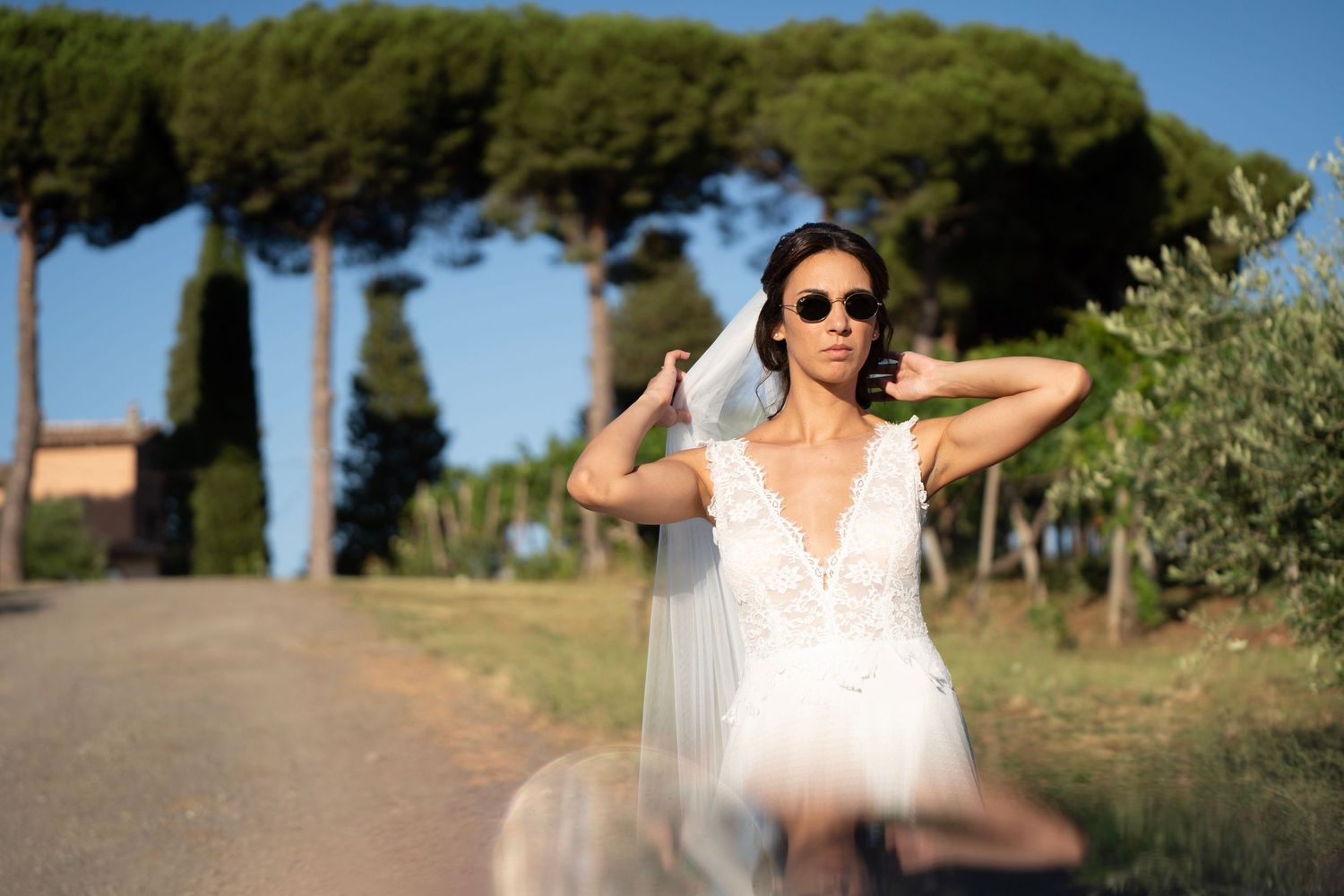 A bride in a flowing white dress poses on a scenic Italian countryside road.
