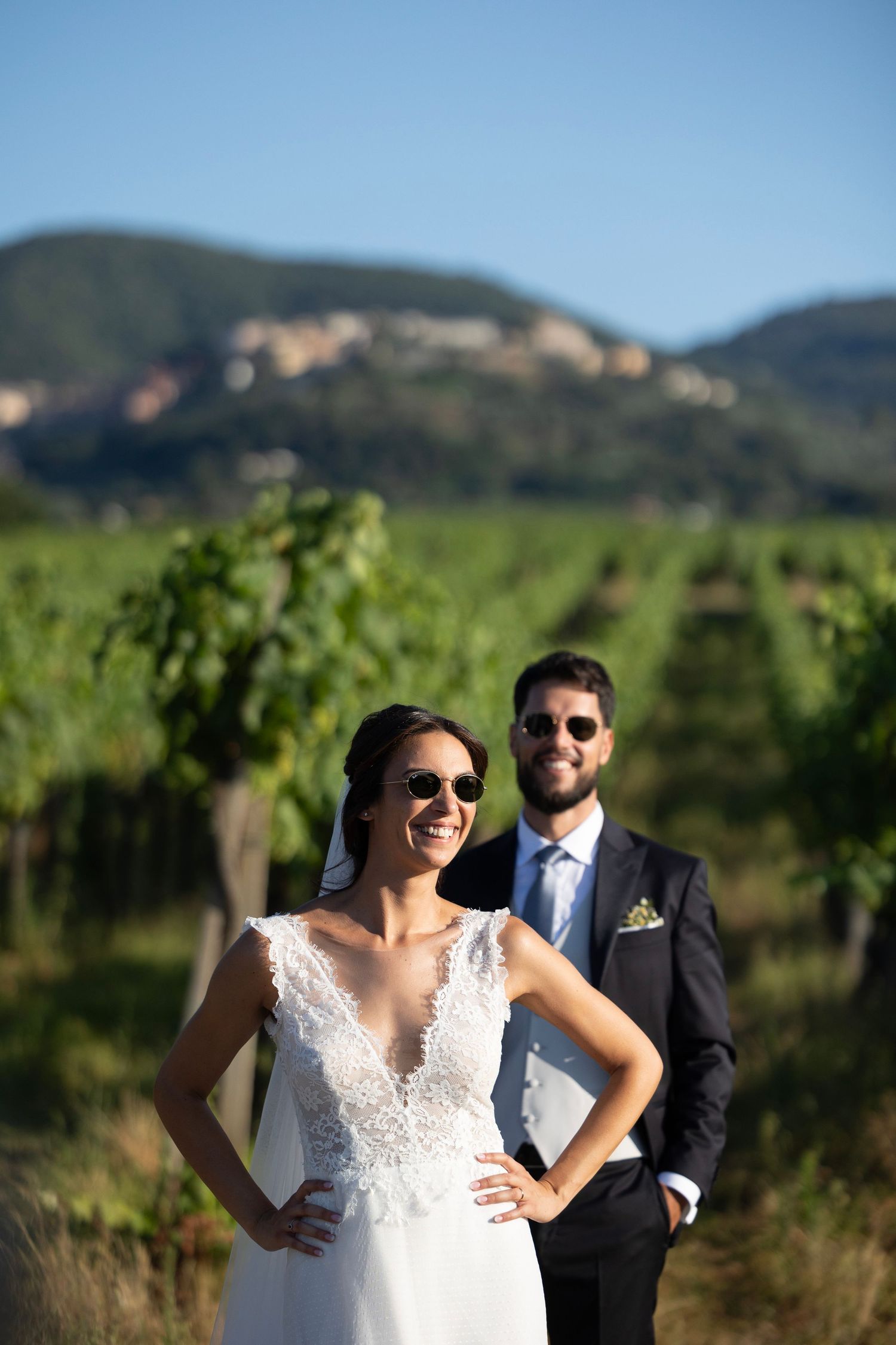 Wedding couple poses in a scenic vineyard with mountains in the background.