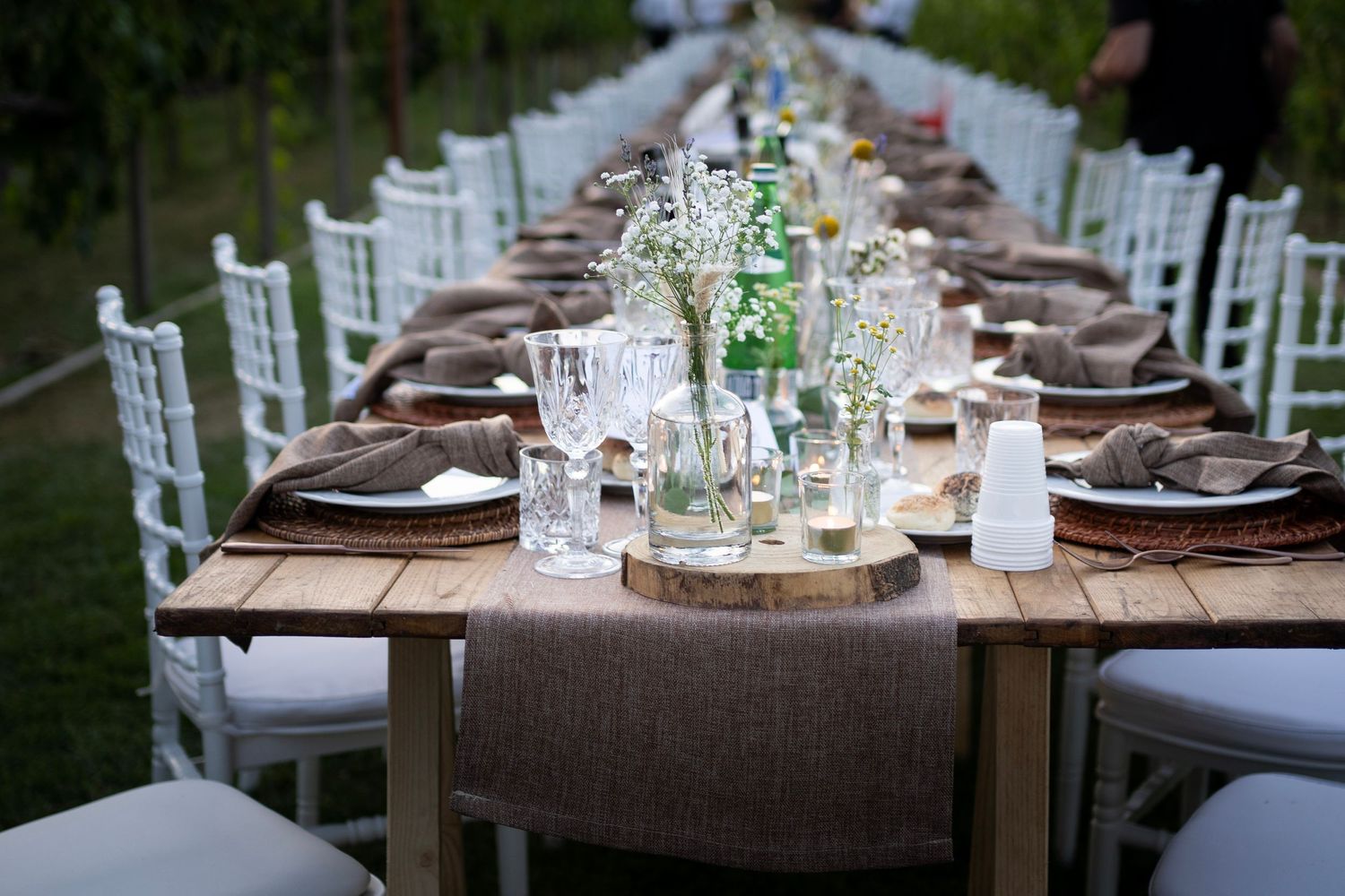 Elegant table setting with white chairs and floral centerpieces in an outdoor vineyard setting.