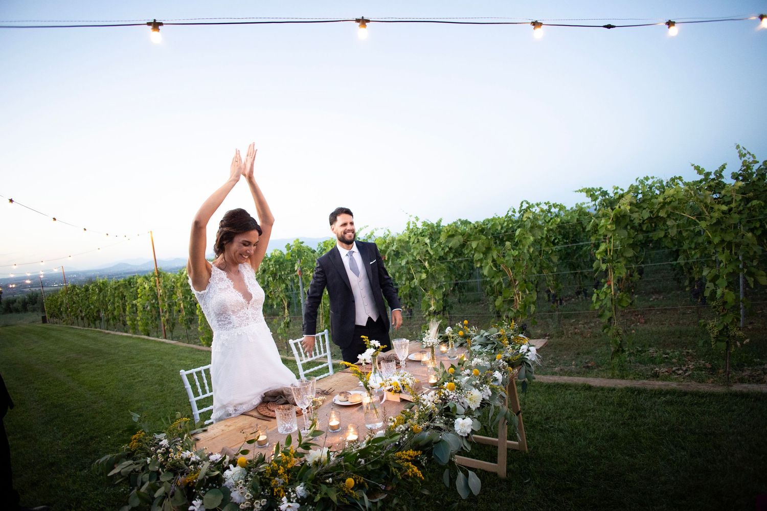 Wedding couple celebrating at their reception table in a vineyard at sunset.
