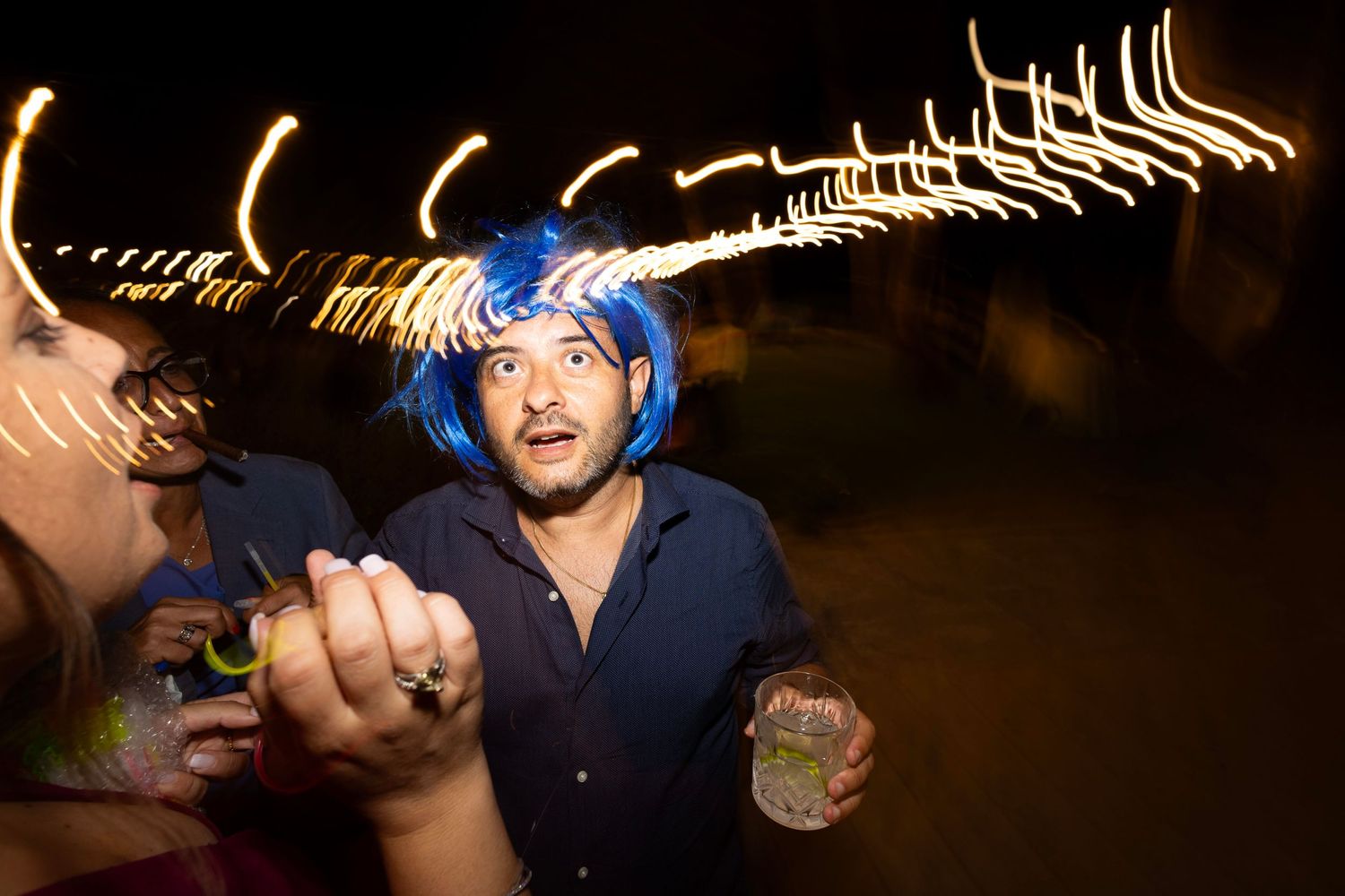 Party guest with blue hair dancing at night with light trails in background.