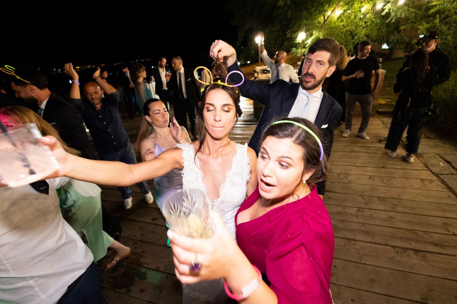 Wedding guests dancing and celebrating with drinks on an outdoor patio at night.