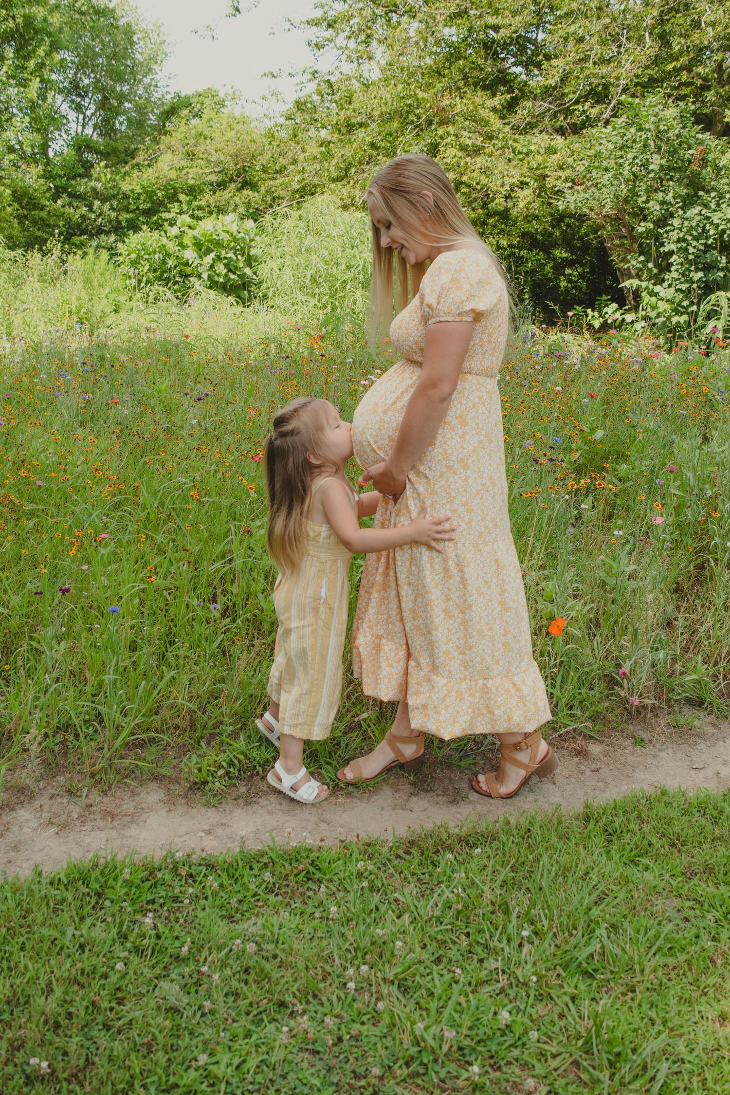 Parent and child in matching floral dresses embrace in blooming wildflower field.