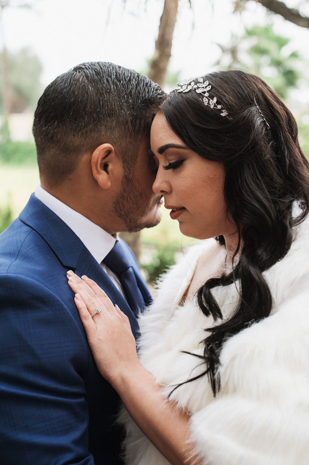 A romantic wedding portrait showing a tender moment between newlyweds, with the bride wearing a fur wrap and crystal headpiece.