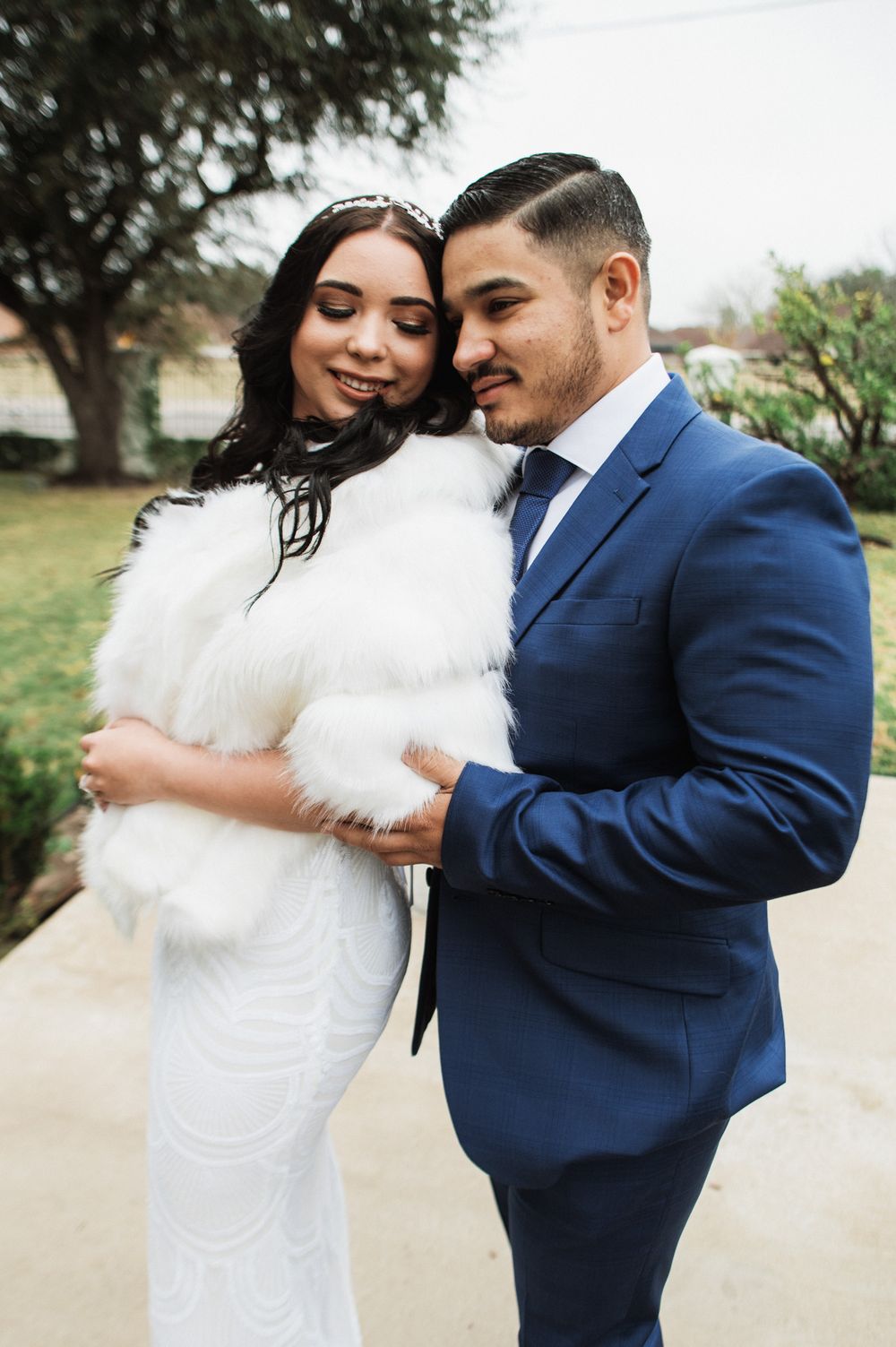 Wedding couple embraces, bride in white fur wrap and groom in navy suit.