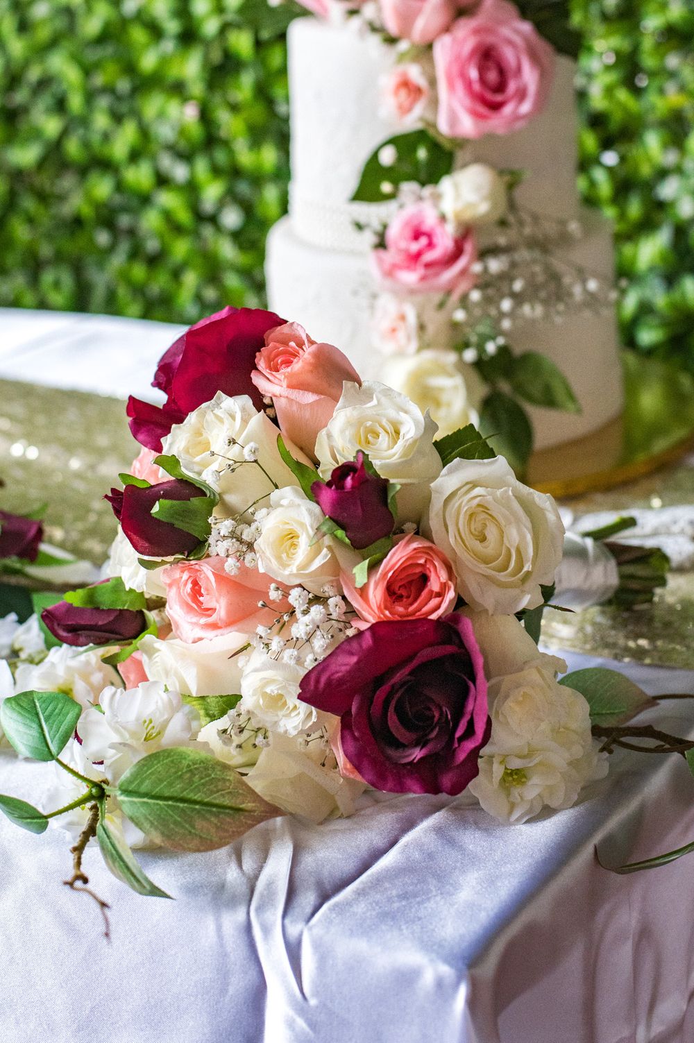 A romantic bouquet of mixed roses in burgundy, pink, and white rests beside a wedding cake.