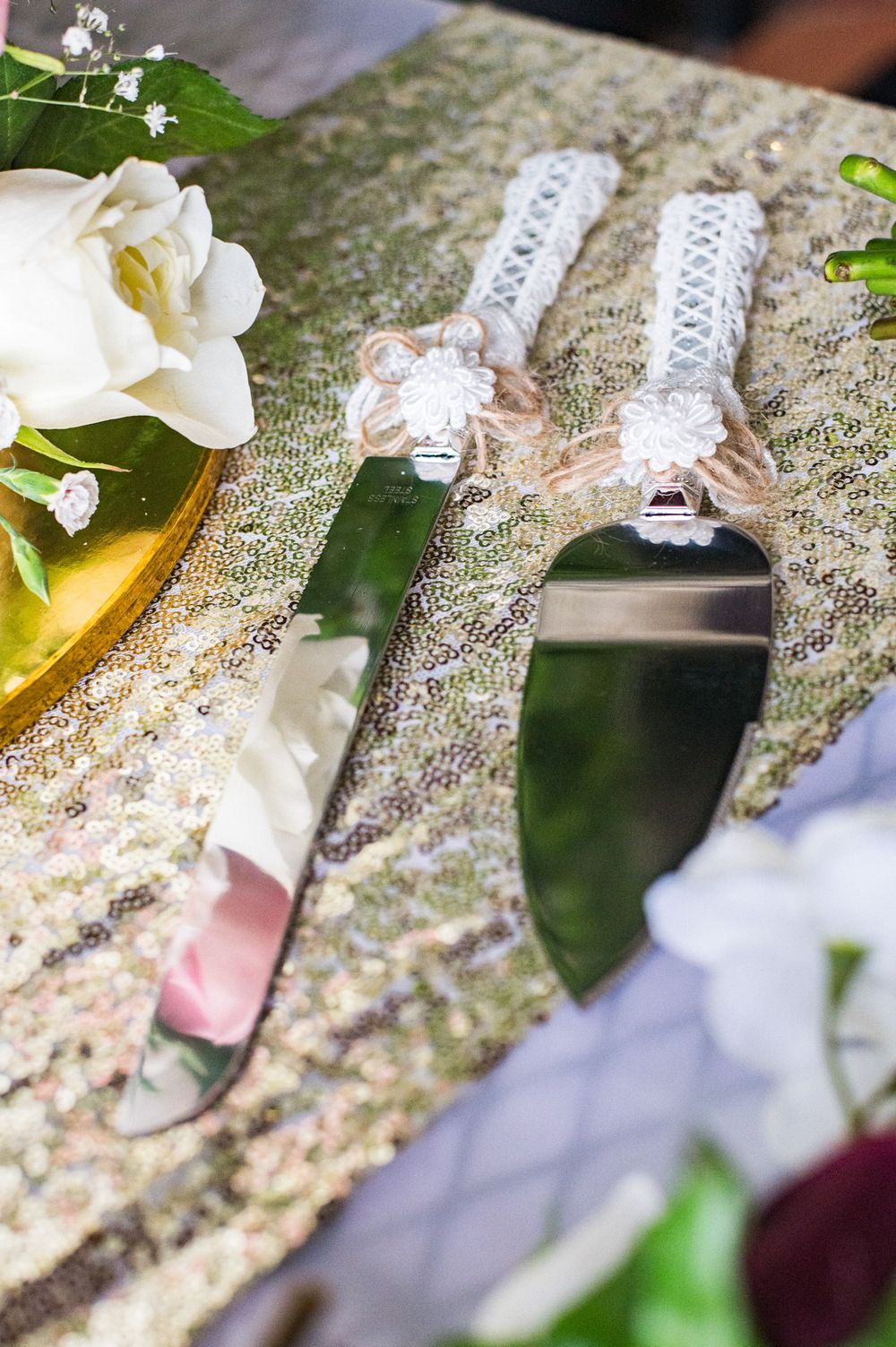 Ornate wedding cake serving set with pearl handles displayed on lace tablecloth with white flowers.