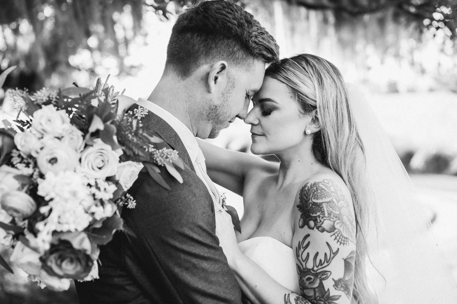 A romantic black and white portrait of newlyweds sharing an intimate moment among floral arrangements.