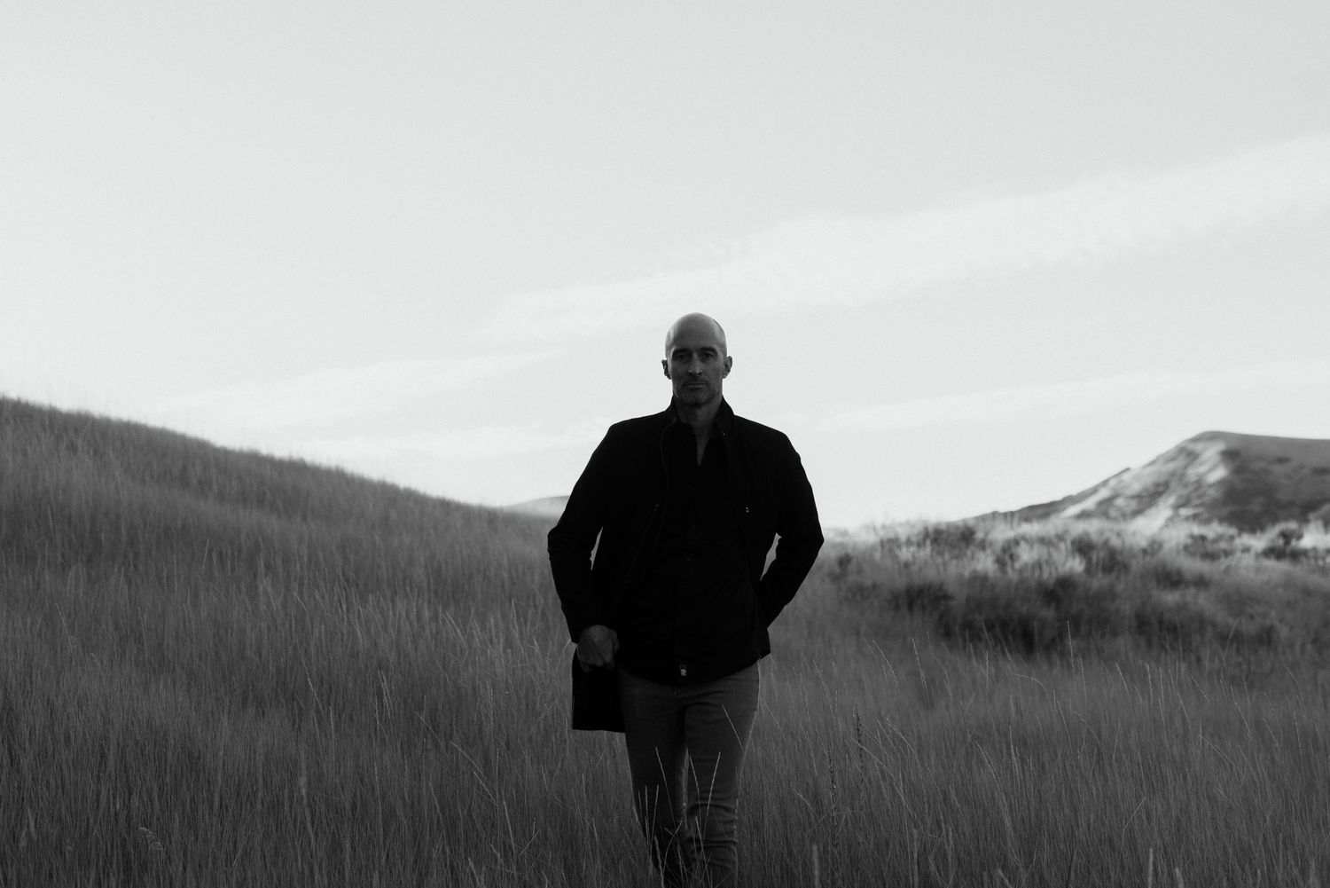 Silhouette of a person standing in tall grass against a mountain backdrop.