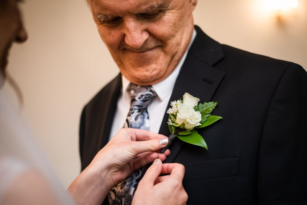 bride pinning boutonniere on father of the bride before wedding ceremony