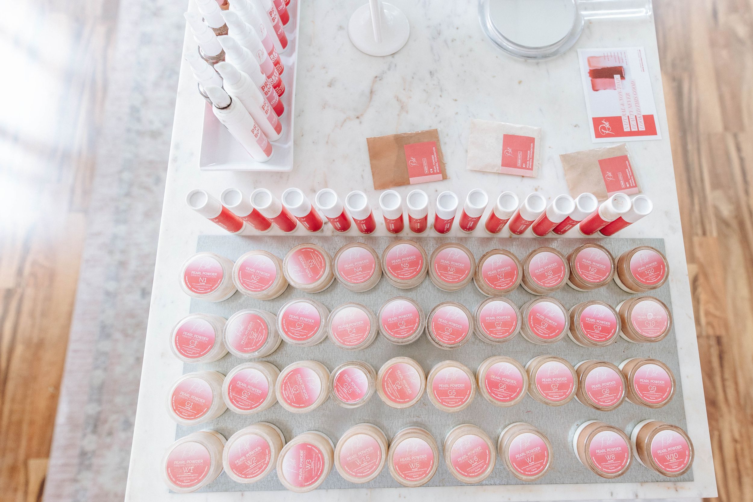 Pink cosmetic product samples arranged in neat rows on wooden surface.