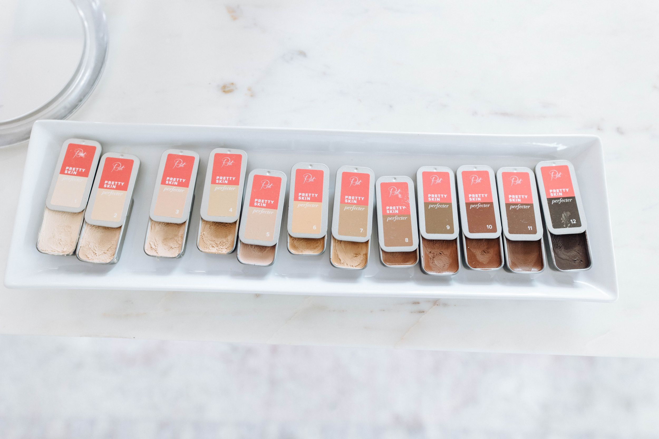 Makeup foundation swatches arranged in a gradient line on white surface.