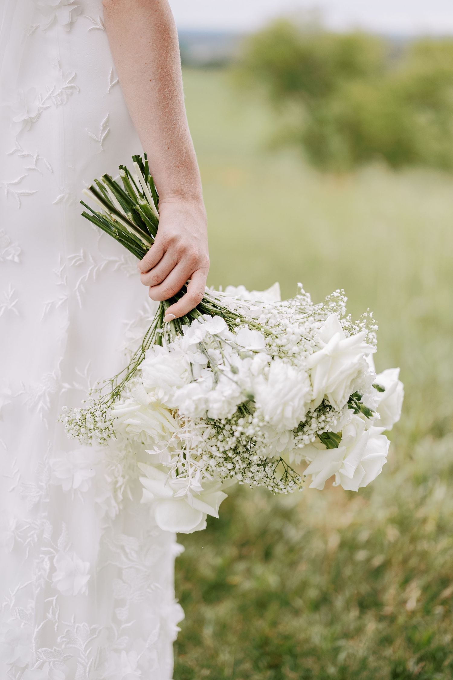 Elegant white bridal bouquet with roses and baby's breath held against a lace wedding dress.
